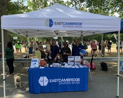 A group of East Cambridge Savings Bank employees standing behind a table with a blue tablecloth at the Hoops and Hope event in Medford