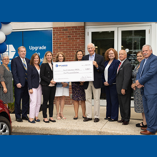 A group of East Cambridge Savings Bank employees and representatives from the North Suburban YMCA hold a ceremonial check and pose for a photo in front of the Bank's new Woburn location.